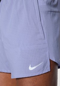 Helllilafarbene Sportshorts aus atmungsaktivem Material, mit kleinen Perforationen und einem weißen Nike-Logo am Saum.