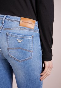 Ljusblå denimjeans med en brun läderetikett från Emporio Armani, silverlogotyp på bakfickan och en figurnära silhuett.