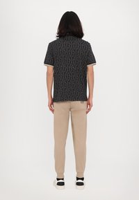 Kortermet svart skjorte med gjentatt tekstmønster, kombineres med beige bukser. Uformell stil, minimal detaljering og en avslappet passform.