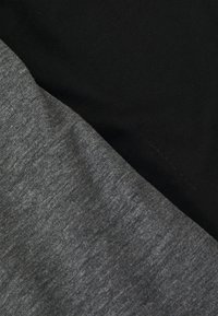 Graue und schwarze Stoffsegmente überlappen sich und zeigen eine glatte Textur sowie ein dezentes Melange-Muster im Grau, mit solidem Schwarz darunter.