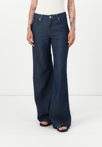 Mørkeblå vide jeans laget av denim, med knappeliv, beltehemper og frontlommer. Glatt tekstur med minimal søm.