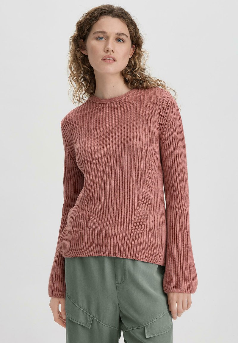 Rosa gerippter Strickpullover mit rundem Ausschnitt, langen Ärmeln und lockerem Schnitt, kombiniert mit olivgrünen Cargo-Hosen.