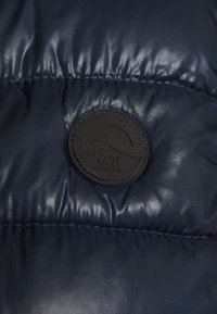 Granatowa puchowa kurtka o błyszczącej, pikowanej strukturze. Posiada okrągłą czarną naszywkę z logo z wzorem góry oraz wypukłym tekstem.