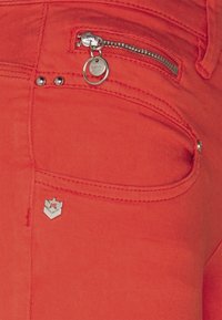 Bright red denim fabric with a small zip pocket and silver hardware. Features metal accents and a logo on the pocket. Smooth texture.