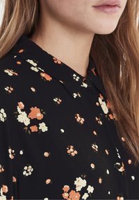 Blusa nera floreale con piccoli fiori arancioni e bianchi, colletto classico e bottoni discreti, realizzata in tessuto leggero.