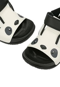 Sandales pour enfants noir et blanc avec un motif de visage de panda sur les brides avant et des brides de cheville noires réglables.