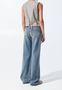 Top sin mangas gris con detalle de lazo en la parte posterior, combinado con unos jeans de pierna ancha azul claro que cuentan con bolsillos traseros y un dobladillo deshilachado.