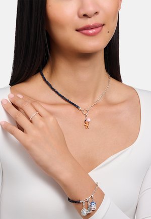 Silberkettencollier mit dunkelblauen Perlen, ausgestattet mit einem Teddybär-Anhänger und einem Armband mit verschiedenen Anhängern und blauen Perlen.