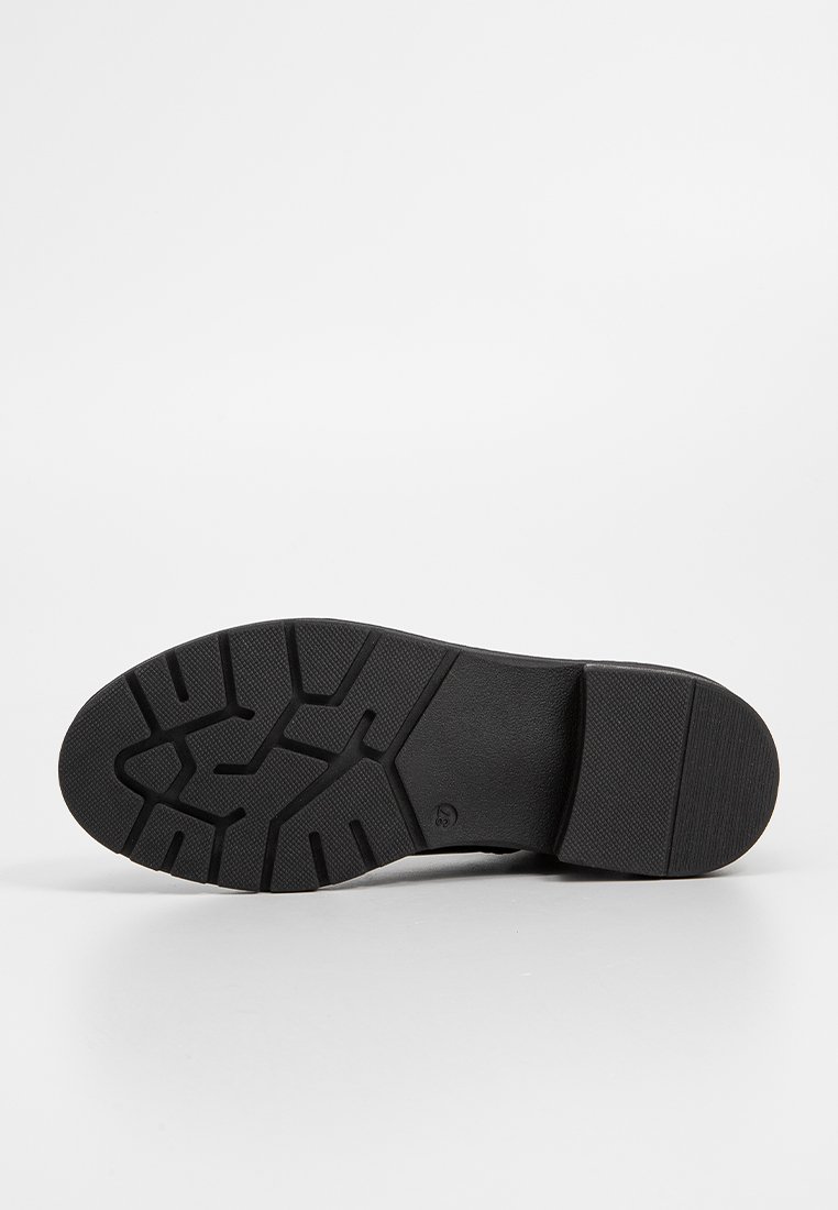 Suela de zapato negra con un patrón de tracción texturizado y una construcción robusta. Superficie lisa con un talón reforzado y material de goma flexible.