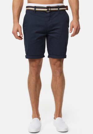 Marineblå shorts lavet af bomuld, med rullet kant, bælte med stribet mønster og frontlommer. Bæres med hvide slip-on sko.