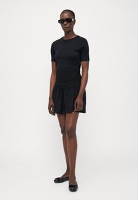 Zwart getailleerd top met korte mouwen gecombineerd met een zwarte uitlopende rok met een textuur elastische tailleband en decoratieve patronen, aangevuld met zwarte flats.