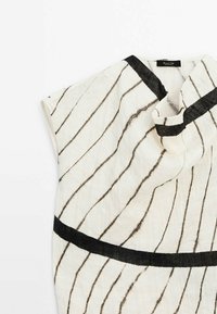 Haut en tissu blanc avec des rayures noires et un col et un ourlet noirs unis. Texture douce avec un design ample et drapé.