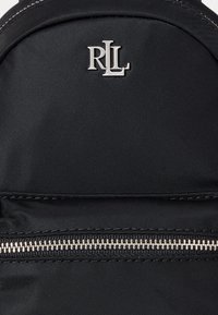 Melnas neilona mugursomas, kurai ir sudraba "RLL" logo un izteikta sudraba rāvējslēdzēja, kas nodrošina drošu aizdarīšanu.