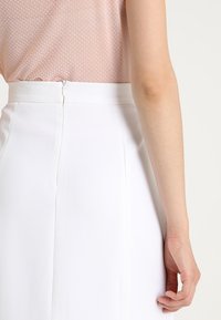 Jupe blanche au toucher lisse et avec une fermeture éclair discrète à l'arrière. La taille est finie de manière soignée, complétant un haut rose pâle avec un motif à pois.