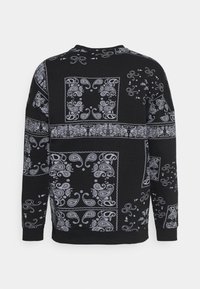 Sudadera negra con patrones de paisley blancos y motivos decorativos a lo largo de la tela. Manga larga, escote redondeado, corte relajado.
