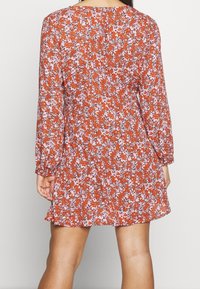 Blommig miniklänning i rödorange med långa ärmar, som pryds av en spridning av rosa och vita blommor på ett lätt och strukturerat tyg.
