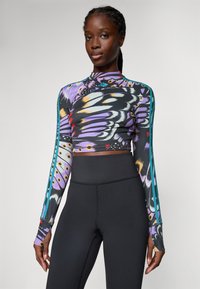 Top scurt cu maneci lungi, decorat cu un imprimeu multicolor de fluturi, având un gât înalt și o croială ajustată. Asortat cu leggings negri cu talie înaltă.