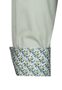 Polsino di camicia verde con un motivo geometrico. All'interno, un motivo floreale con accenti blu, verdi e neri su uno sfondo bianco.