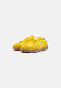 Żółte zamszowe sneakersy z zaokrąglonym noskiem, sznurowanym zapięciem, białym akcentem na pięcie oraz gumową podeszwą z teksturowanym wzorem.