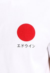 Fehér pamut póló, amelyen egy nagy piros kör és alatta fekete japán szöveg található. Egyszerű dizájn, sima textúrával.