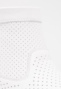 Chaussure en cuir blanc à tige haute, avec des perforations pour la ventilation et une surface texturée. Accents cousus autour des bords.