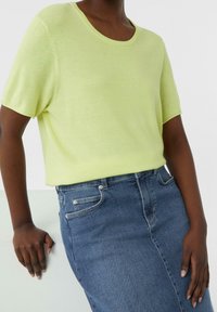 Jersey de manga corta verde lima hecho de un tejido suave, combinado con una falda de mezclilla oscura que presenta un diseño clásico de cinco bolsillos.