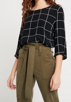 Czarna bluzka z długim rękawem w biały wzór w kratę, wpuszczona w oliwkowe spodnie z wysokim stanem, wyposażone w szeroki materiałowy pasek związany w talii.