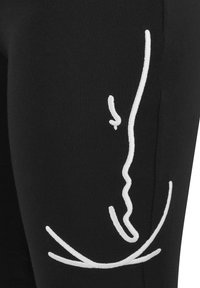 Tissu noir avec un art linéaire minimaliste blanc représentant un profil de visage sur le côté d’un vêtement.