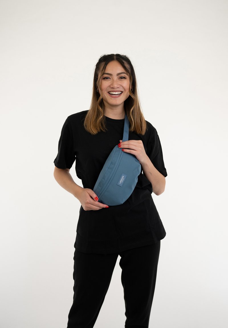 Tökéletes zöld, szövet övtáska cipzárral és állítható pánttal. Téglalap alakú, sima textúrájú, elöl márka címkével.