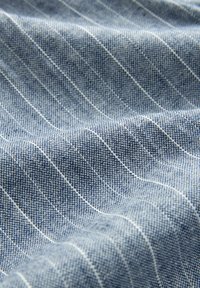 Denimstoff mit hellblauen und weißen vertikalen Streifen, ausgestattet mit einer strukturierten Webart und einer weichen, glatten Oberfläche.