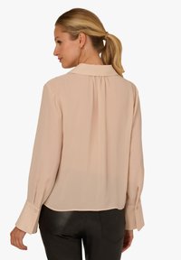Light pink blouse with long sleeves, a back pleat, a collared neckline, and buttoned cuffs. Smooth texture with a relaxed fit.