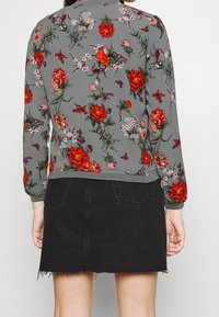 Szary sweter z kwiatowym wzorem w czerwone i różowe kwiaty, połączony z czarną spódnicą dżinsową z postrzępionym dołem i dwiema tylnymi kieszeniami.