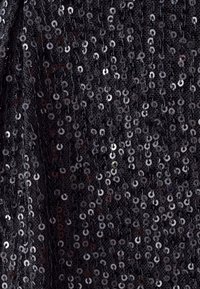 Tessuto nero con paillettes, caratterizzato da un denso motivo di paillettes rotonde, che crea una superficie testurizzata e lucente con una leggera brillantezza.