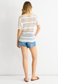 Hvid åbenstrik sweater med korte ærmer, prydet med blå horisontale striber, parret med denim shorts og brune slide sandaler.