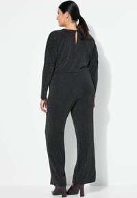 Mono negro de manga larga, con textura brillante, detalle de apertura en la espalda y diseño de pierna ancha. Combinado con tacones burdeos brillantes.