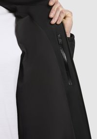 Black jacket featuring a side zippered pocket, smooth texture, and a fitted design. Lined interior with hood detail visible.
