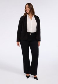 Černý blazér over bílou košilí s jemnými puntíky. Černé široké kalhoty se zlatými knoflíky. Modelka v černých lodičkách.