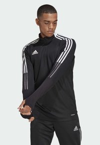 Schwarzes sportliches Halbzip-Oberteil mit langen Ärmeln, ausgestattet mit drei weißen Streifen auf jeder Schulter, aus leichtem Stoff mit Daumenlöchern.