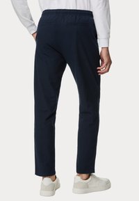 Pantaloni blu navy dal taglio rilassato con vita elasticizzata, due tasche posteriori e una texture simile a un tessuto intrecciato. Indossati con sneakers bianche.