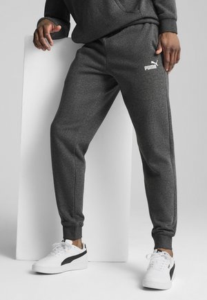 Grijze fleece joggers met elastische boorden en zijzakken; voorzien van een wit Puma-logo op de linkerdij. Gecombineerd met witte sneakers.