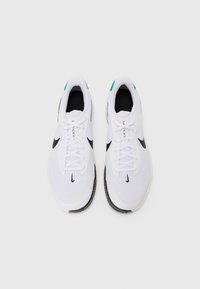 Hvide atletiske sko med en tekstureret mesh-overdel, sort Nike swoosh-logo og teal accenter på hælen. Har flade snørebånd og gummisål.
