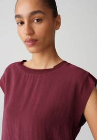 Top bordeaux con maniche corte, realizzato in un tessuto morbido e texturizzato, con scollatura rotonda. Un leggero lucido arricchisce il design.