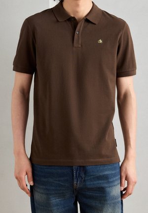 Polo marrone in cotone morbido con patta a tre bottoni, maniche corte, discreto logo e orlo dritto, abbinato a jeans blu.