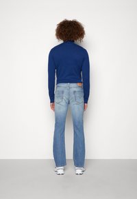 Jersey de tortuga azul combinado con jeans acampanados de color azul claro. El jersey es ajustado, los jeans tienen un diseño clásico de cinco bolsillos con costuras visibles.