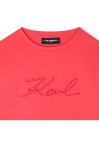 Rød bomulls-T-skjorte med rund hals og brodert "Karl"-logo i en matchende rød nyanse. Jevn tekstur, avslappet design.