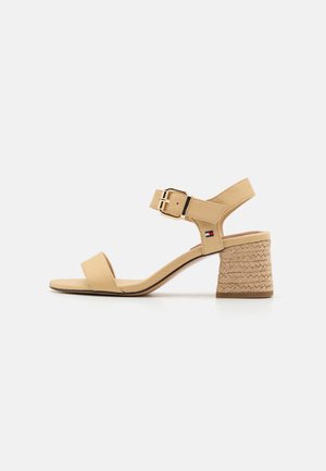 Sandales à talons hauts beiges avec un talon bloc tressé, une bride de cheville réglable et une tige en cuir lisse. Détail boucle dorée.