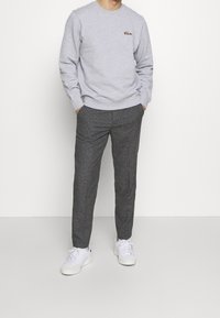 Felpa grigia con polsini e orlo a coste, abbinata a pantaloni grigi scuri testurizzati e sneakers bianche, dotata di un piccolo logo sul petto.