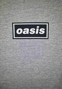 Grå t-shirt med et sort rektangulært logo med ordet "oasis" i hvid, centralt placeret, lavet af blødt bomuldsstof.