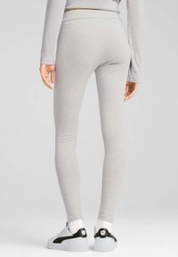 Graue Leggings aus dehnbarem Material, enganliegendes Design, glatte Textur, mit hohem Bund und kombiniert mit weißen und schwarzen Plateausneakern.