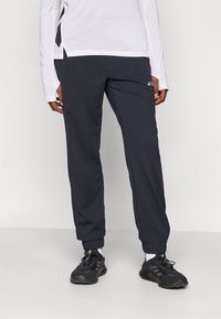 Schwarze Sporthose mit elastischem Bund, Bündchen am Knöchel und dezentem Logo-Detail am Bein, kombiniert mit dunklen Laufschuhen und weißen Socken.